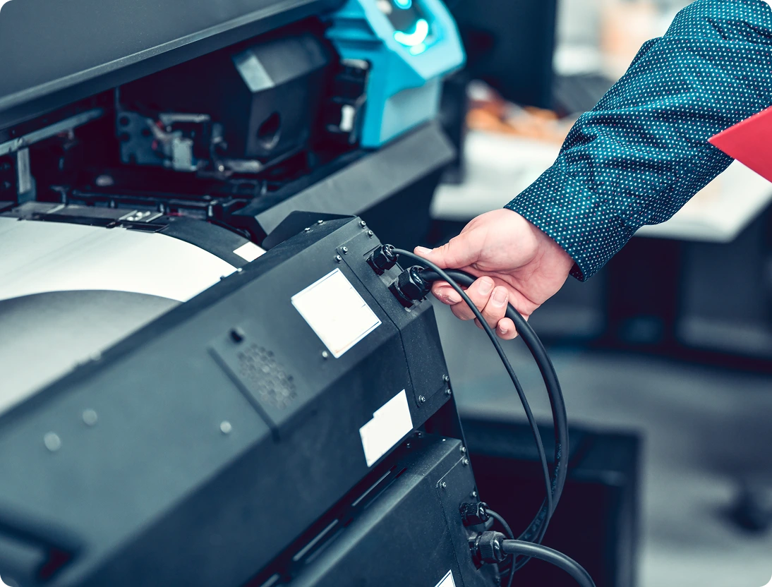Person connecting cables to a printing machine.